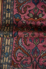 Folded corner of a Persian rug revealing the gem-toned fuchsia arabesques and short-pile texture.