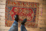 Vintage Anatolian rug section with cherry red field, sapphire blue border, and visible wear. Black boots.