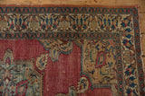 Corner of antique Doroksh rug showing detailed meandering vine border, faded cochineal red field.