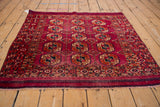Angled view of a vintage Turkmen square rug with repeating elephant footprint guls on a fuchsia field.