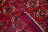 Construction detail of a vintage Turkmen rug with a folded corner showing the magenta pile and striped ends.