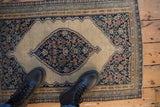 Antique Persian Senneh rug with navy Herati medallion on an expansive beige field.