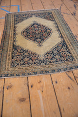 Antique Senneh rug corner featuring navy Herati design, beige field, and patterned borders.
