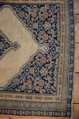 Antique Senneh rug corner spandrel with navy Herati motifs, beige field, and geometric border.