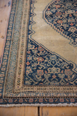 Corner of antique Senneh rug with Herati design motif and navy, beige patterned borders.