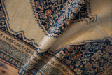 Antique Senneh rug's folded texture, displaying navy stepped medallion, Herati design, and beige field.