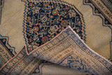 Antique Senneh rug corner showing folded foundation, fringed edge, and navy Herati motif on beige.