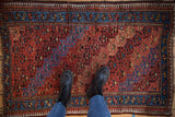 Vintage Kurd rug with an abrashed red field and blue geometric border, viewed from overhead.