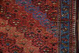 Close-up of a vintage Kurd rug's worn pile, showing the knot heads, red field, and blue border.