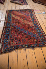 Angled profile of a vintage Kurd rug with an abrashed red field and blue pawn motif border.