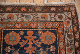 Vintage Hamadan rug corner, navy field, terracotta and ivory borders, stylized shrubs, worn fringe.