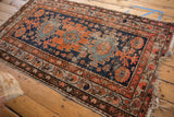 Corner view of vintage Hamadan rug, with navy and terracotta borders, intricate patterns, and tattered fringe.