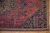 Vintage Senneh rug corner detail with raspberry red field, navy Herati spandrel, and seed border.