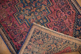 Vintage Senneh rug's folded corner reveals red pile, fringe, and reverse with glue remnants.