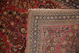 Corner of a vintage Sarouk rug, showing dusty red floral pile and intricate geometric border weave.