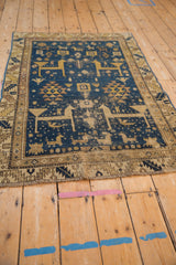Fringe and geometric animal motifs with foundation wear on a deep blue Caucasian rug.