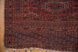 Vintage Turkmen rug corner shows light fringe, black cherry red field, navy hook-and-latch borders, even wear.