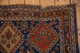Geometric corner and dark fringe of an antique Persian Qashqai rug with low, hand-knotted pile.