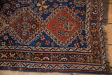 Corner view of an antique Qashqai rug showing the geometric borders, wide selvage, and dark fringe.