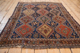Angled view of a square antique Qashqai rug showing its repeating geometric panels and low pile texture.