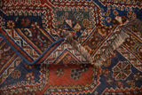 The folded corner of an antique Qashqai rug reveals its wool pile, fringe, and bold blue selvage.
