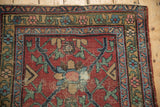 Heriz rug corner detail: black cherry red geometric field, gold and blue borders, visible pile wear.