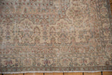 Distressed vintage Kerman carpet corner detail with faded floral arabesques, visible foundation, and fringe.