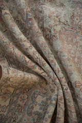 Close-up of distressed Kerman carpet showing muted floral arabesques and foundation wear.