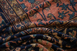 Folded vintage Mahal carpet reveals dusty rose, navy, and teal scrolling motifs.