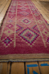 Angled view of a distressed Kurd runner emphasizing its gem-like magenta color and repeating diamond medallions.