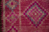 Evenly worn low pile of a distressed rug in magenta, ivory, and slate blue.