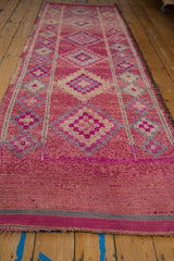 A perspective view of a distressed Kurd runner showing its abrashed magenta field and diamond pattern.