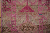 Close-up of vintage distressed Kurd rug with fuchsia motifs, muted background, and textured wear.