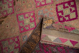 Folded Vintage Distressed Kurd rug with geometric fuchsia blossoms and textured beige pile revealing foundation.