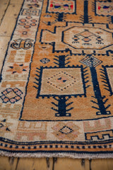 Detail of a vintage distressed Kurd rug's secured fringe and geometric border in tangerine, navy, and ivory.