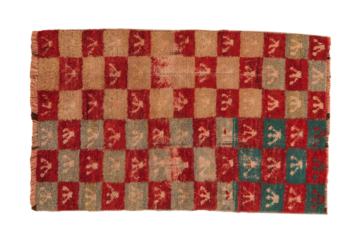 A distressed vintage Tulu rug with a shaggy checkerboard pattern of red, beige, and turquoise trefoil motifs.