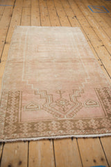 Angled view of a distressed Oushak rug's geometric prayer motif in dusty blush and brown.