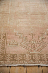 Low pile texture and geometric border motifs in dusty blush and coffee brown on a vintage rug.