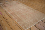 Angled view down the length of a distressed Oushak prayer rug in faded dusty rose and beige.