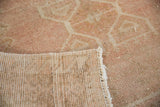 Folded corner of a distressed Oushak rug showing its dusty rose pile and hand-knotted foundation.