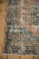 Distressed Hamadan rug corner showing faded beige, seafoam, and brown tones with exposed foundation.