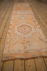 Geometric medallions and distressed texture of a vintage Kurd runner in orange, ivory, and beige.