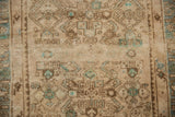 Distressed texture of the Hamadan rug's worn pile, with beige, brown, and celadon Herati details.