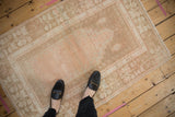 Scale view of a small distressed Oushak rug with a faded dusty rose and beige palette.