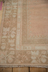 A distressed Oushak rug corner with a worn, hand-knotted pile and beige floral border.