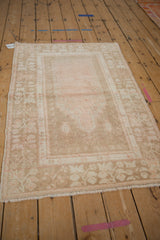 Long angled view of a distressed Oushak rug showcasing its faded dusty rose field and beige floral border.