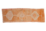 Vintage distressed Kurd runner rug in pale rust, tangerine, and faded magenta diamond medallions.
