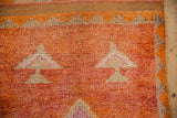Vibrant orange and ivory geometric motifs on a distressed Kurd rug's textured pile.