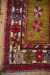 Corner of vintage Oushak rug, unusual moss green field, cherry red border, vibrant floral motifs with wear.