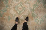 Feet on a distressed vintage Kars carpet, showing muted geometric patterns in dusty green and sand.